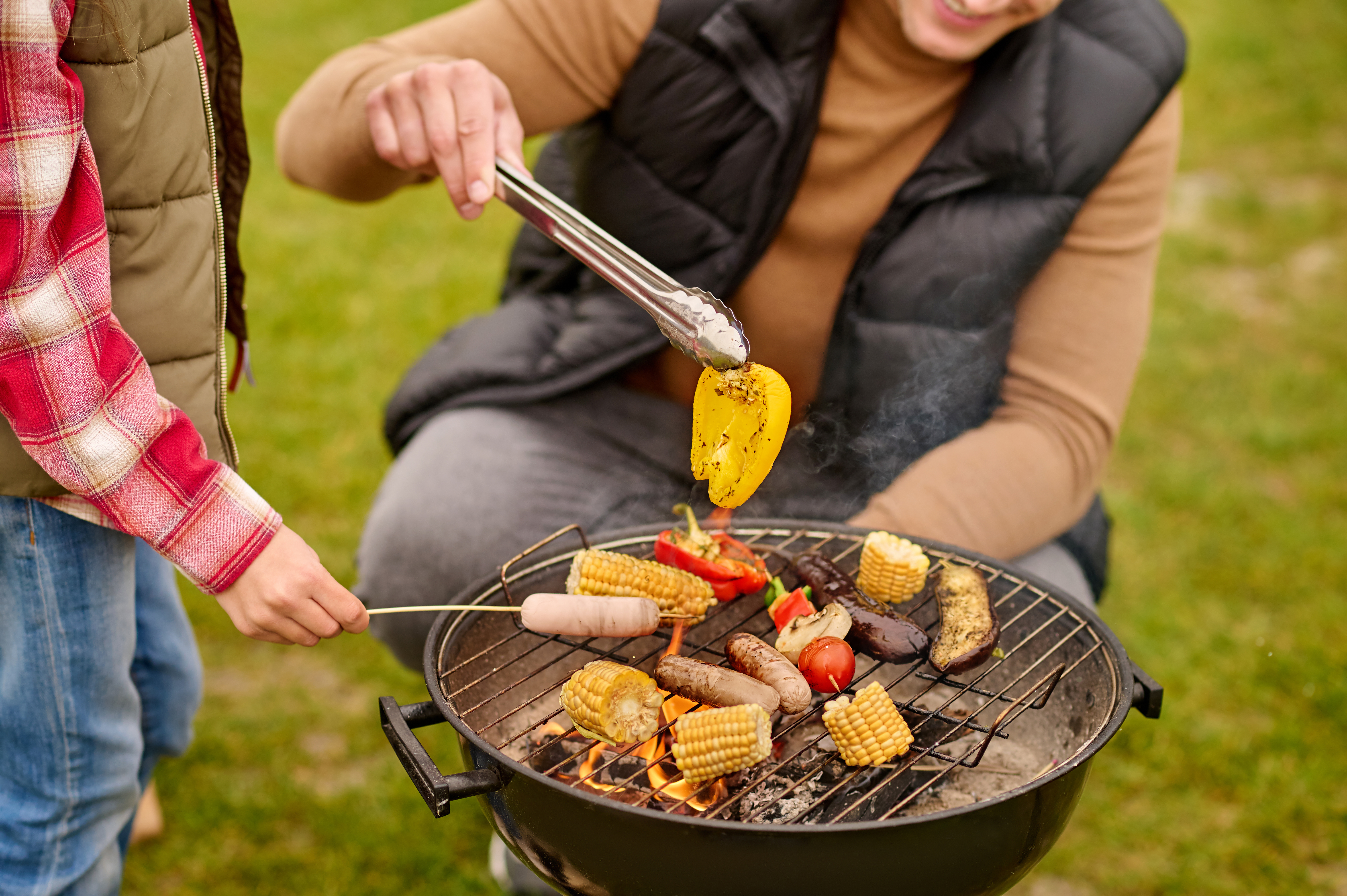 Man crouched near barbecue with vegetables